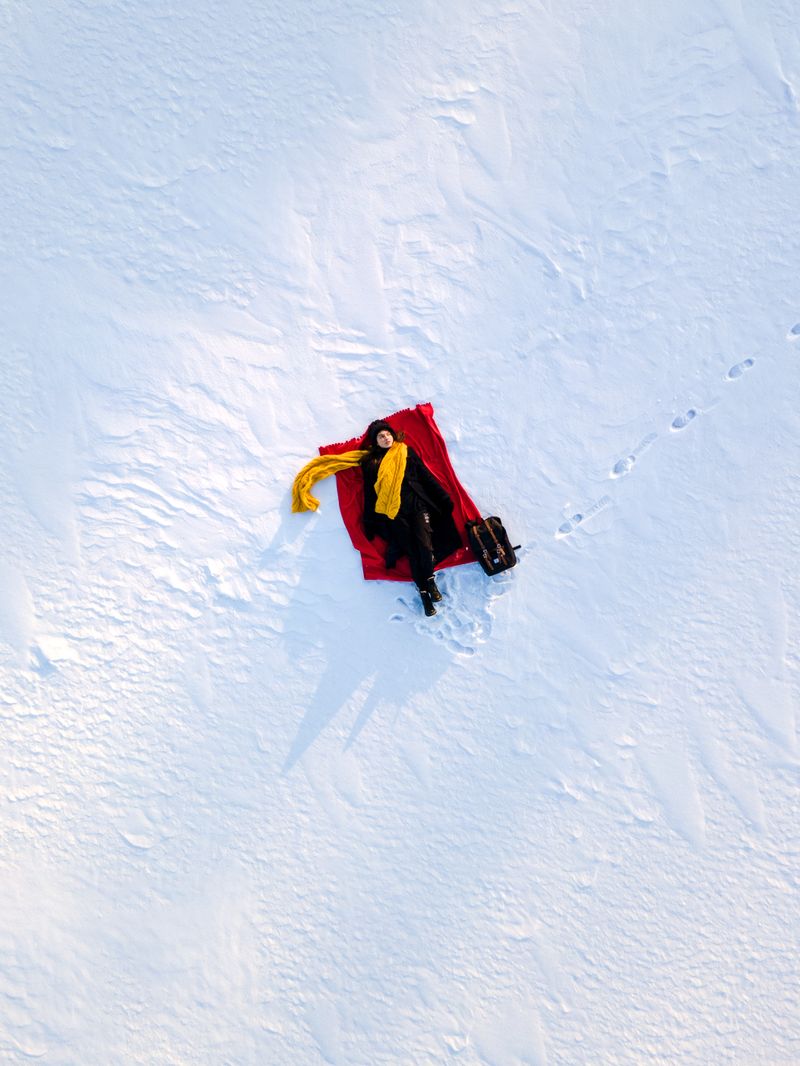 Woman in coat with yellow scarf on red blanket in snow