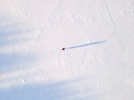 Drone shot capturing a solitary figure walking across a vast snow-covered landscape.