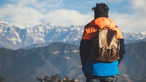 Free Man With Backpack Looking At Snow Covered Mountains Stock Photo