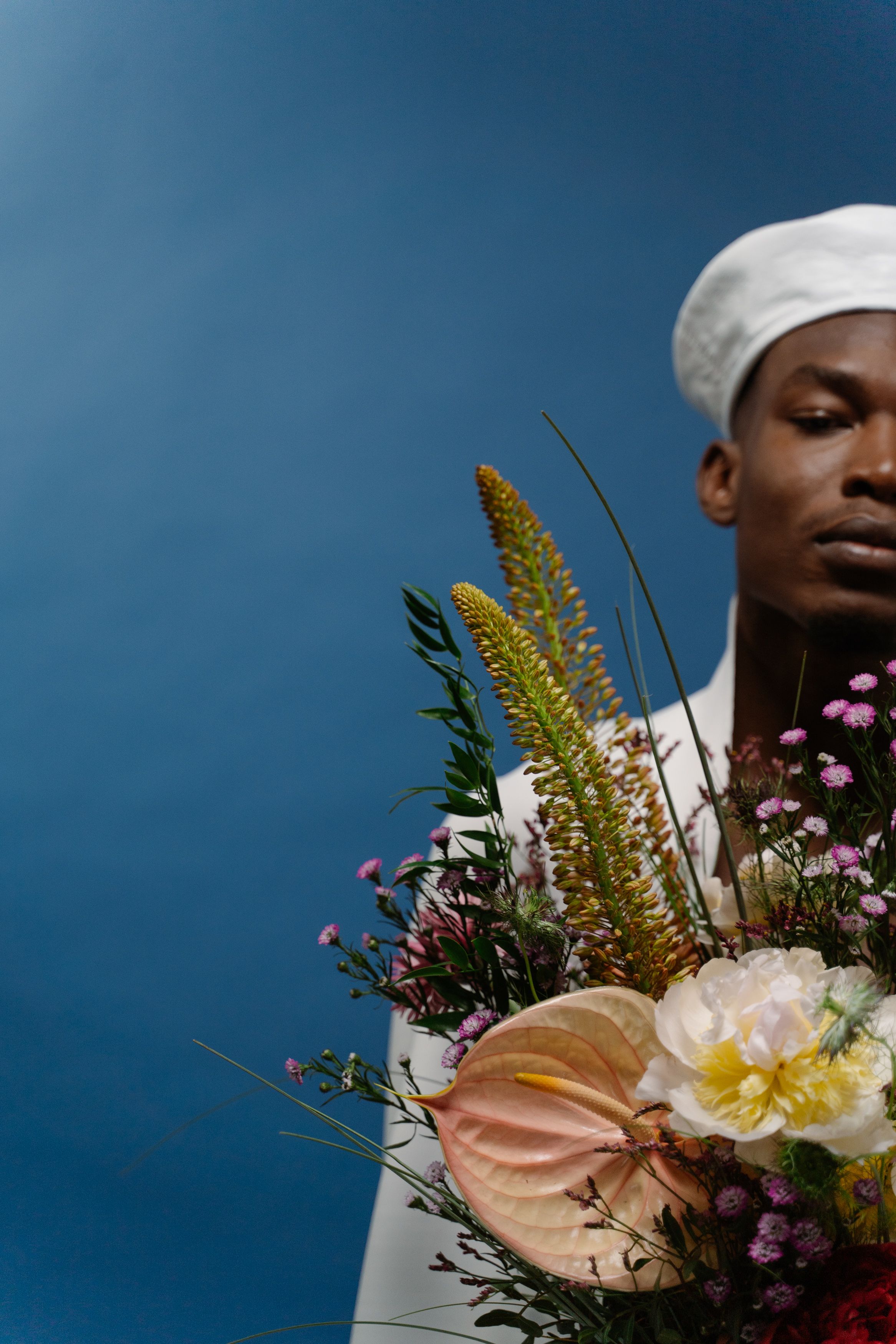 A man elegantly holding a vibrant bouquet against a blue backdrop.