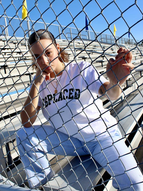 Free 
A Woman Wearing a White Shirt and Denim Pants Holding on a Chain Link Fence Stock Photo