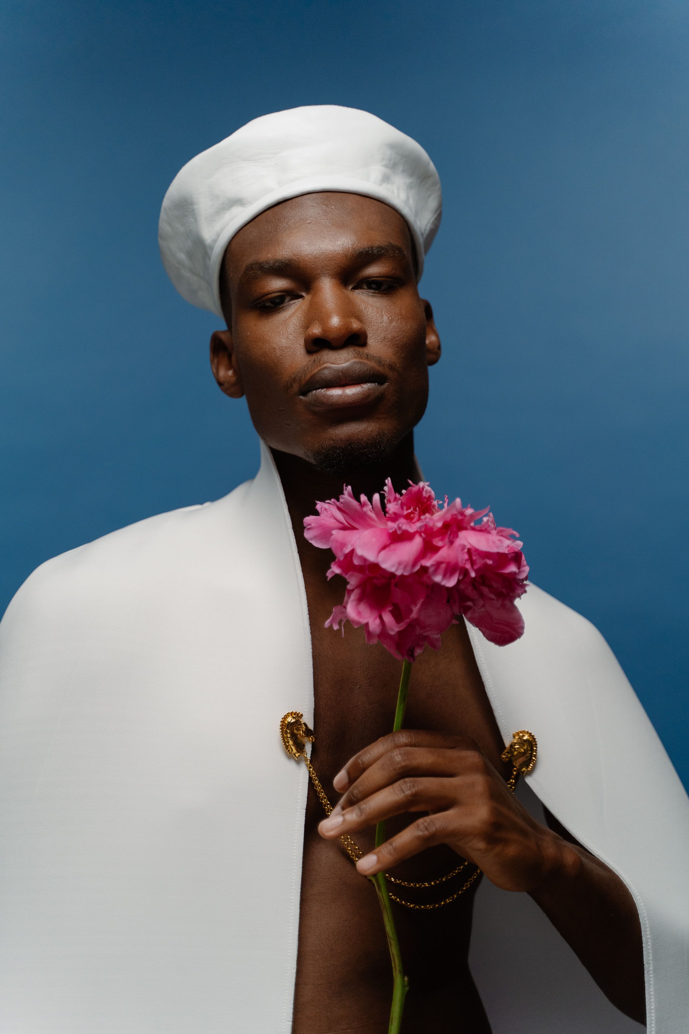 Elegant portrait of a stylish man in a white cape holding a vibrant pink flower.
