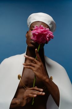 A creative fashion portrait featuring a model with a pink peony against a blue background.