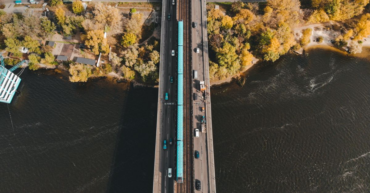 Aerial shot of a bridge over River Dnipro in Kyiv with cars and a train traversing in autumn.