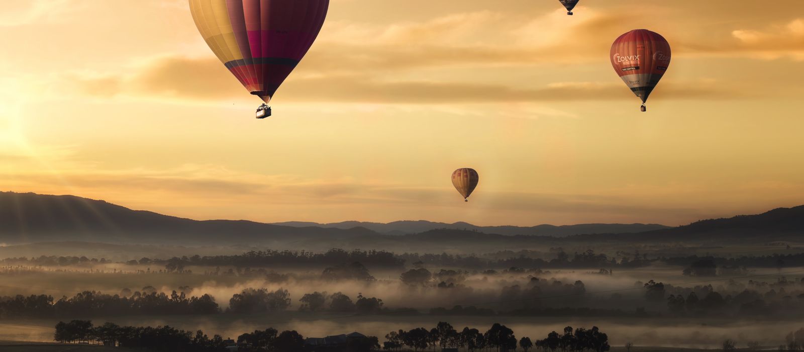 Hot air balloons floating over misty fields at sunrise, creating a picturesque adventure scene.