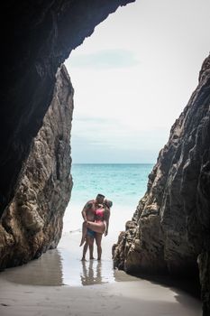 A couple embracing by the ocean in a secluded beach cave setting.