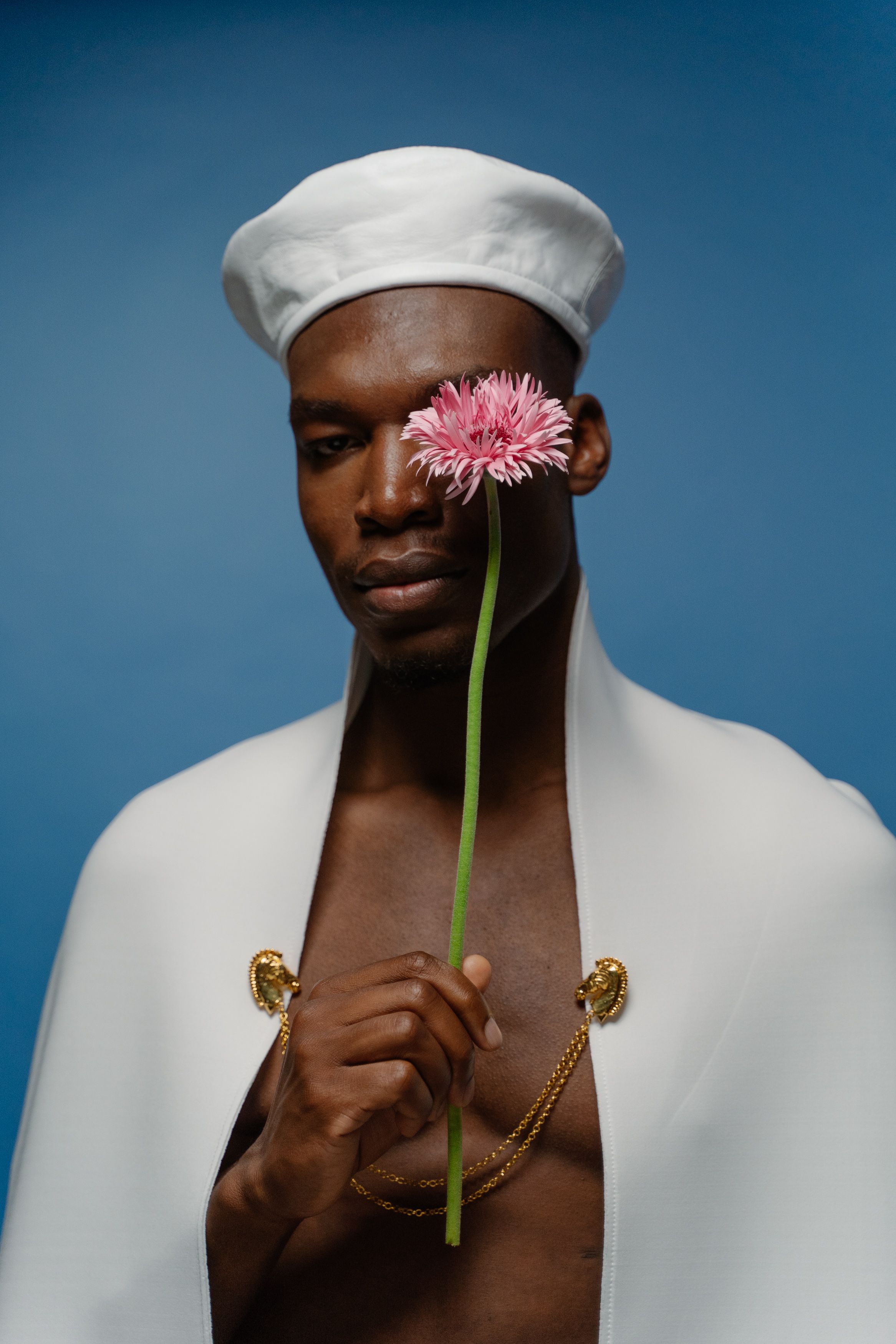 Portrait of a stylish man in white cape and hat holding a pink flower.