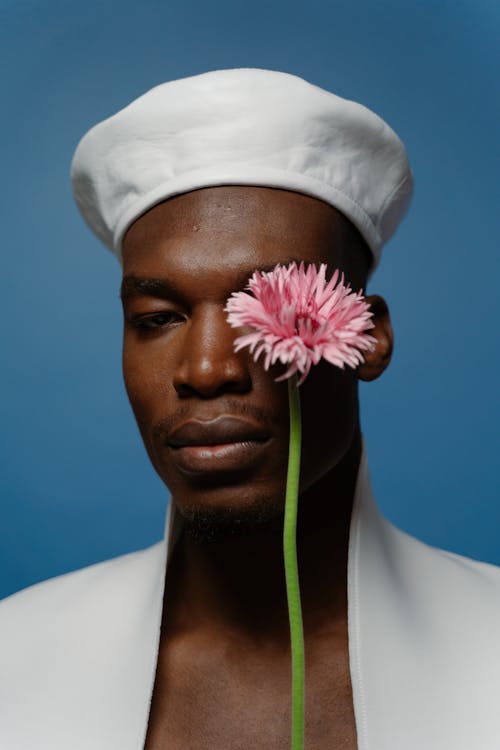 
A Man Wearing a Hat Holding a Stem of Flower