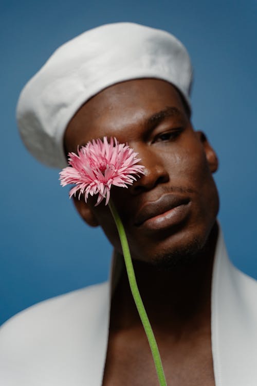 
A Man Wearing a Hat Holding a Stem of Flower