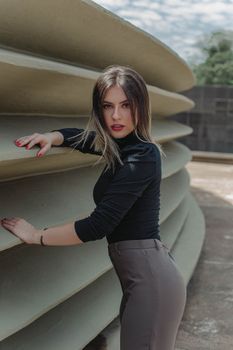 Stylish young woman with brown hair posing elegantly outdoors next to an architectural structure.
