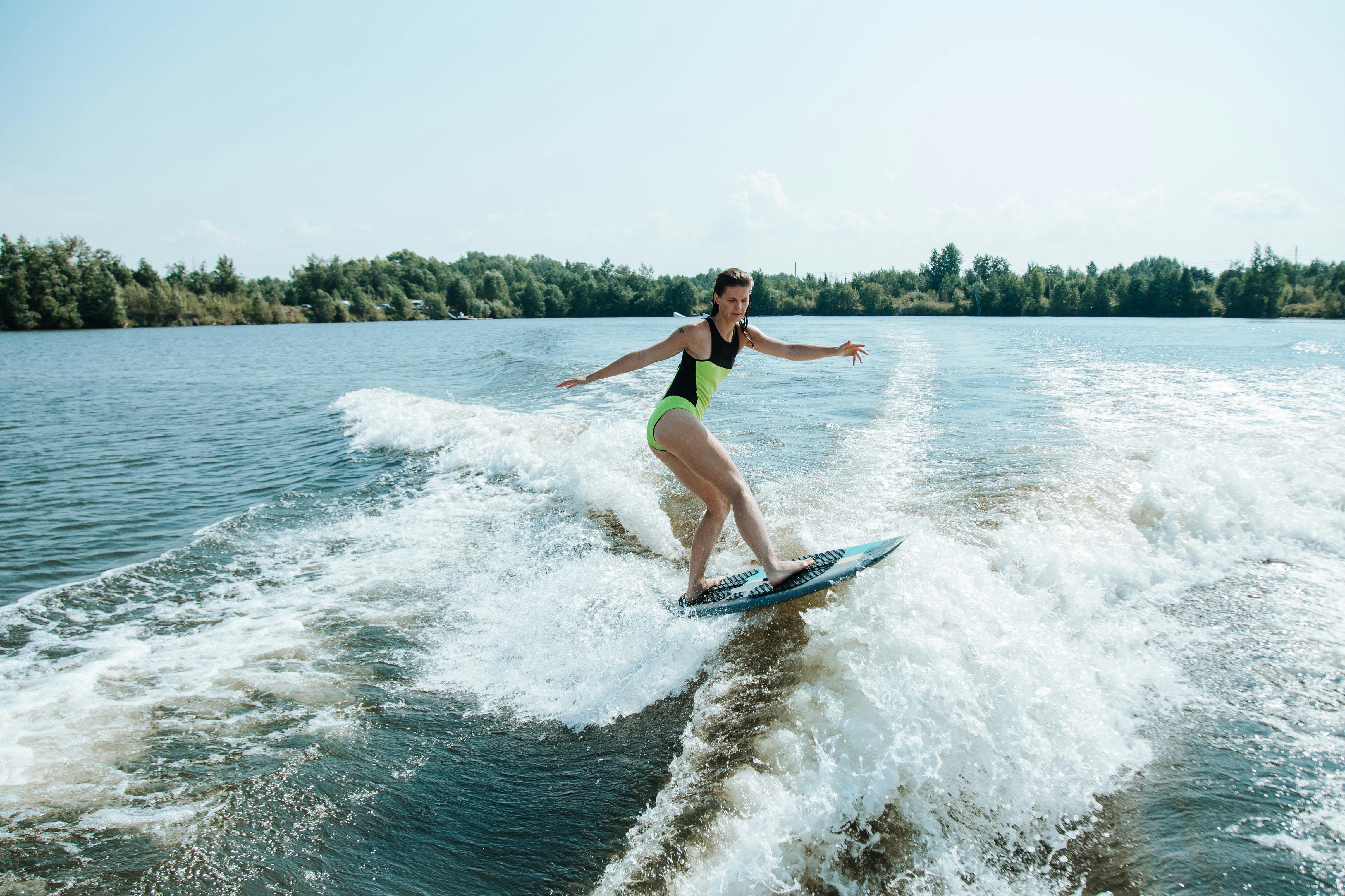 woman wakesurfing on lake surrounded by forest