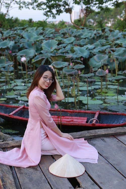 Free A Woman Wearing a Pink Ao Dai Kneeling on a Wooden Bridge Stock Photo