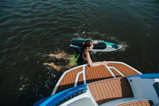 A woman with surfboard in water beside a boat on a sunny summer day.