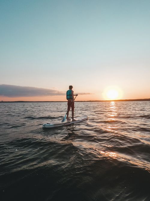 Free Man paddleboarding at sunset on a tranquil lake, capturing the essence of adventure and serenity. Stock Photo