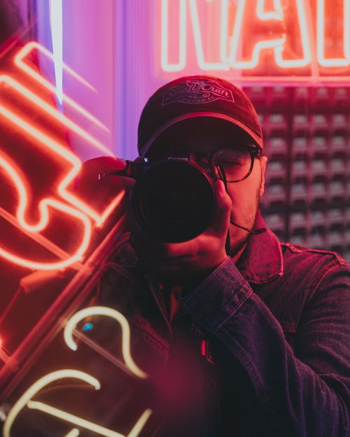 Free Portrait of a man capturing urban nightlife surrounded by vibrant neon signs. Stock Photo