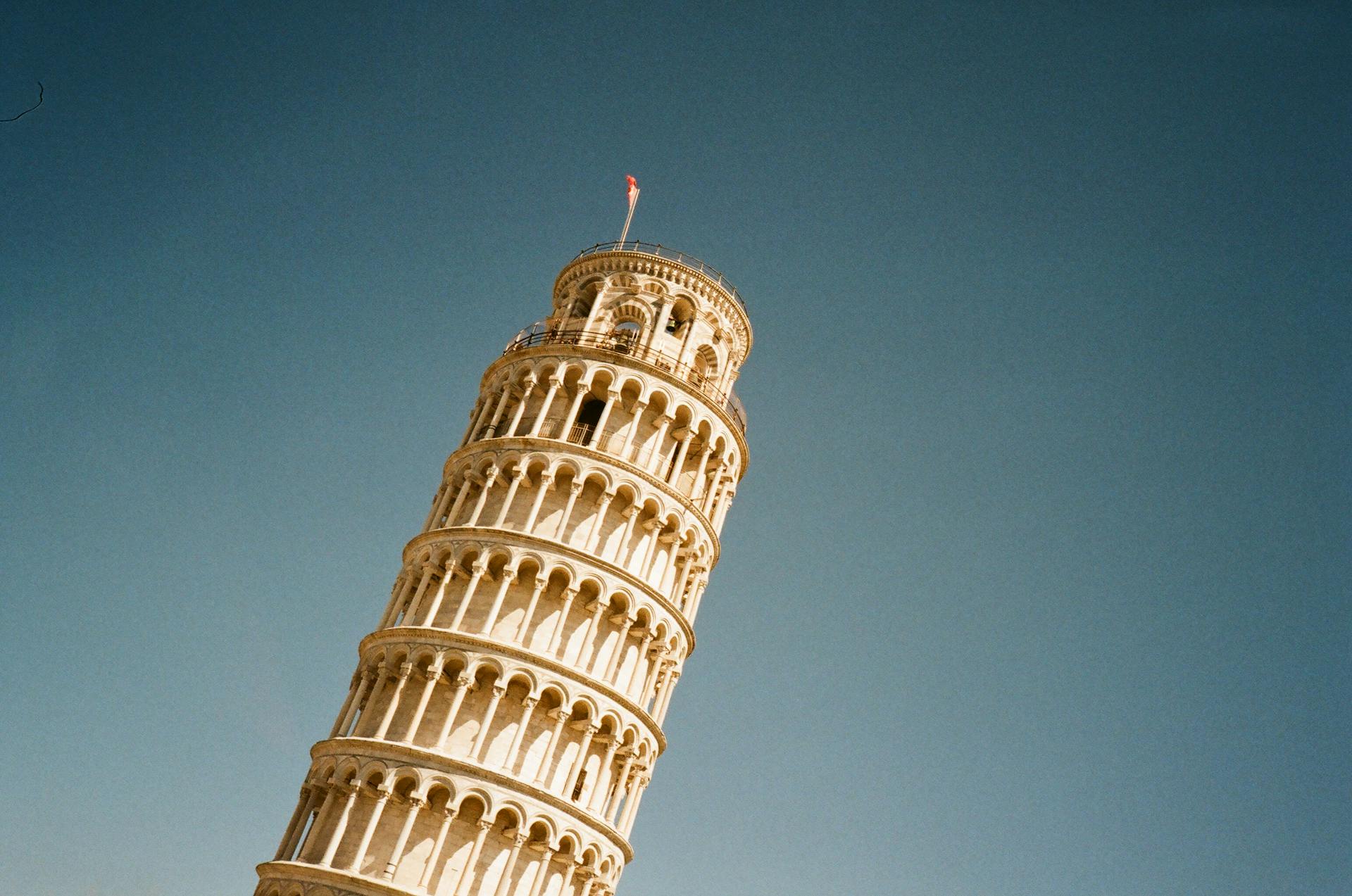 Iconic low angle view of the Leaning Tower of Pisa with a clear blue sky overhead, emphasizing its architectural beauty.