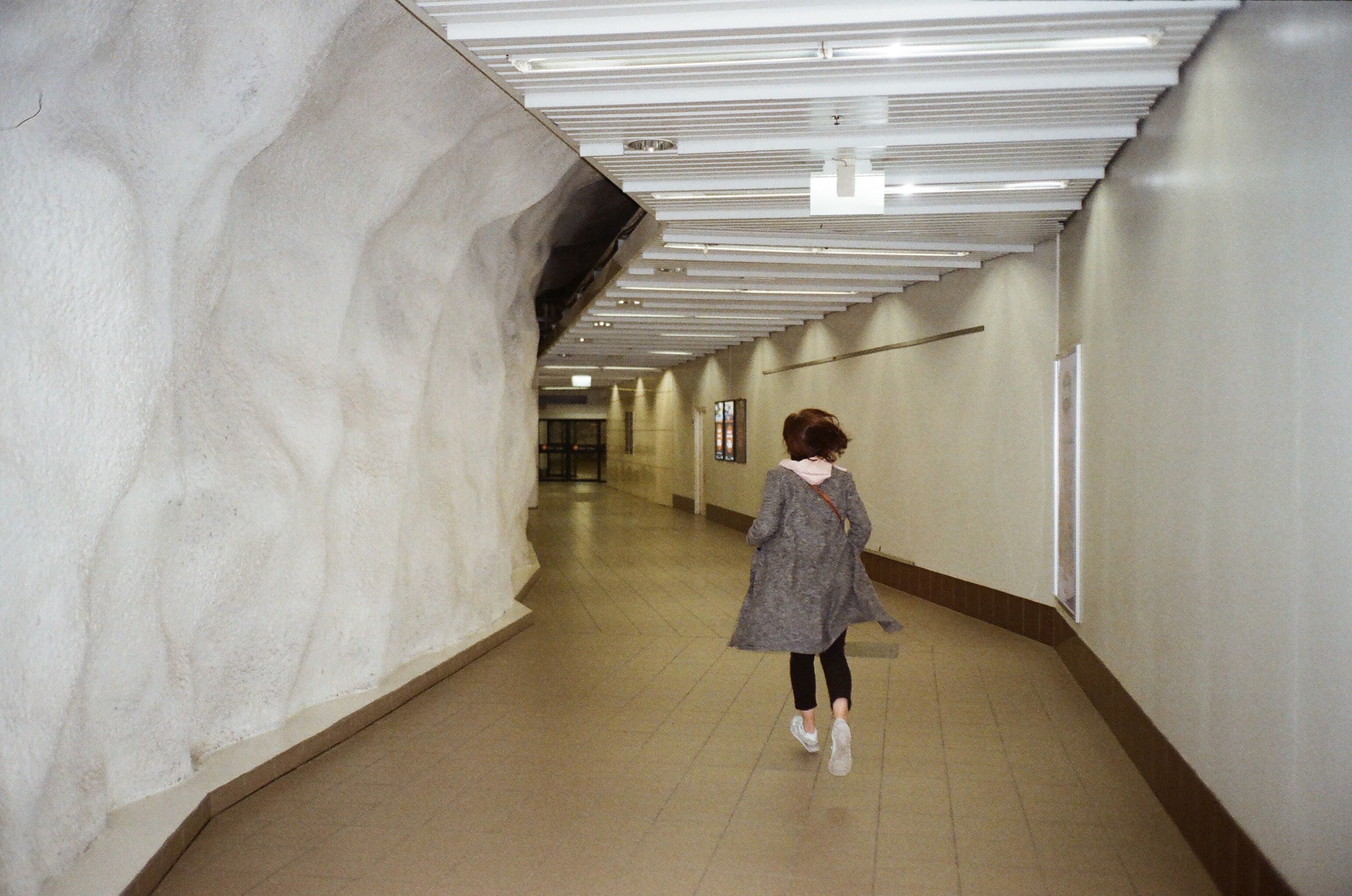 A woman in a trench coat runs through a modern underground tunnel in Helsinki, Finland.