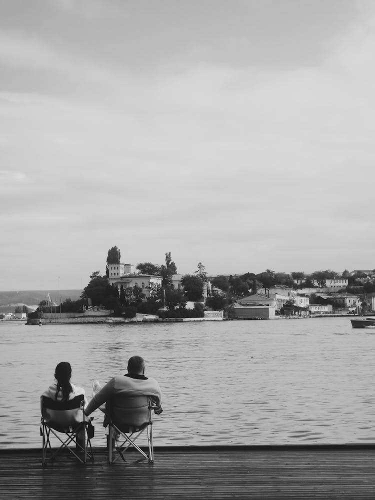 Grayscale Photo Of A Couple Sitting On Folding Chairs