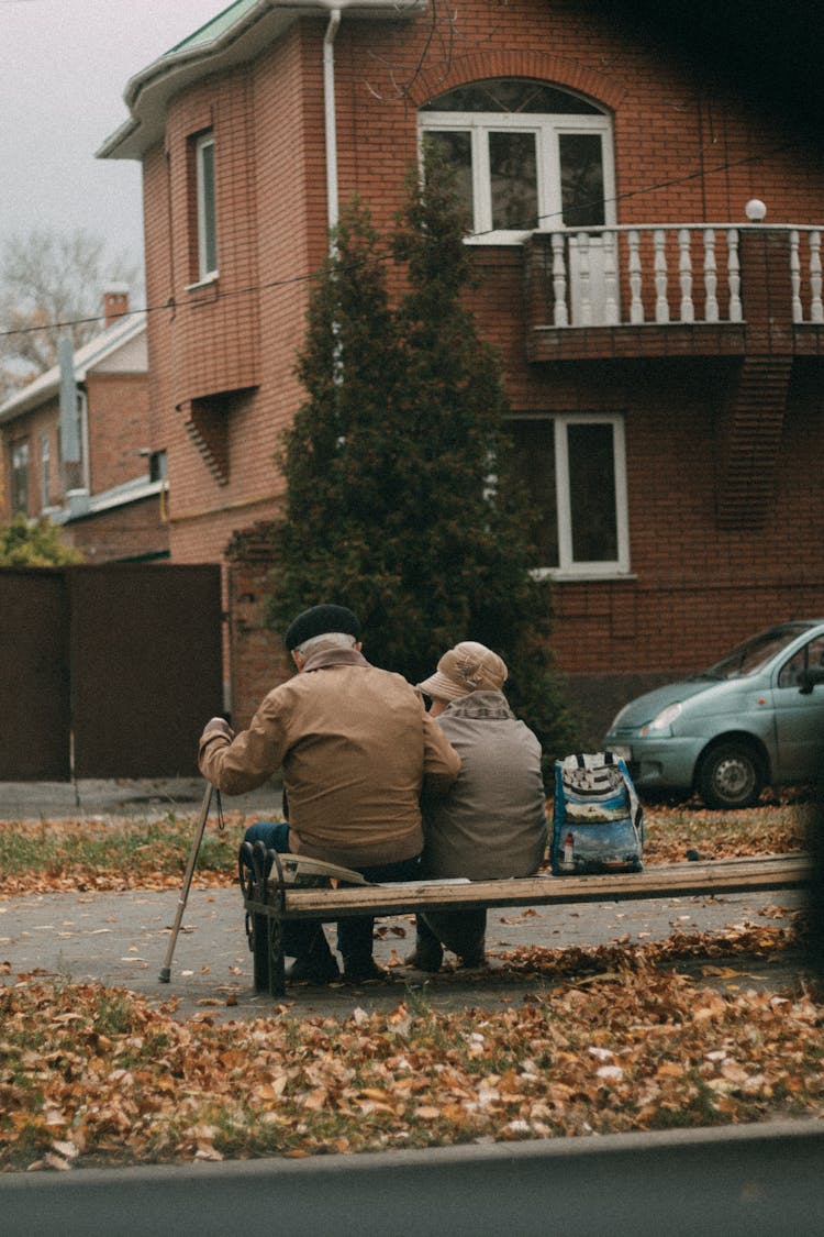 Back View Of An Elderly Married Couple Sitting On A Bench