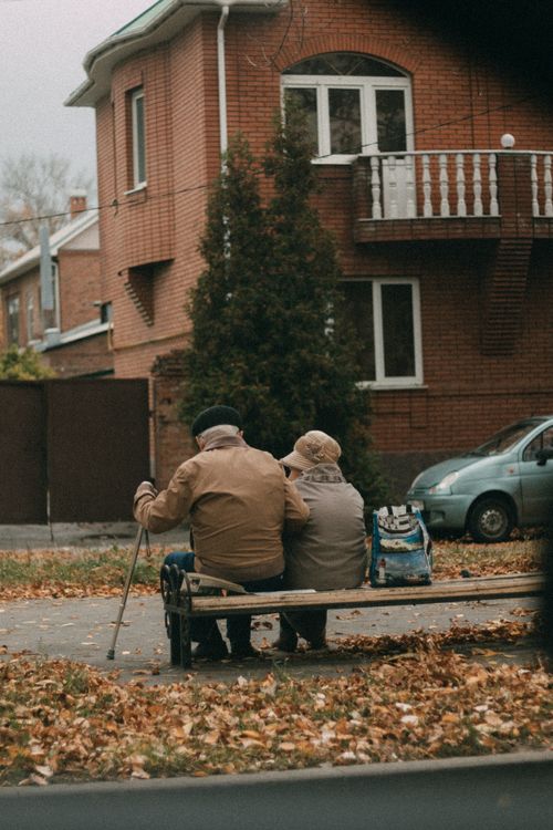 Free Elderly couple enjoying a quiet moment together on a bench surrounded by fallen leaves in an urban setting. Stock Photo