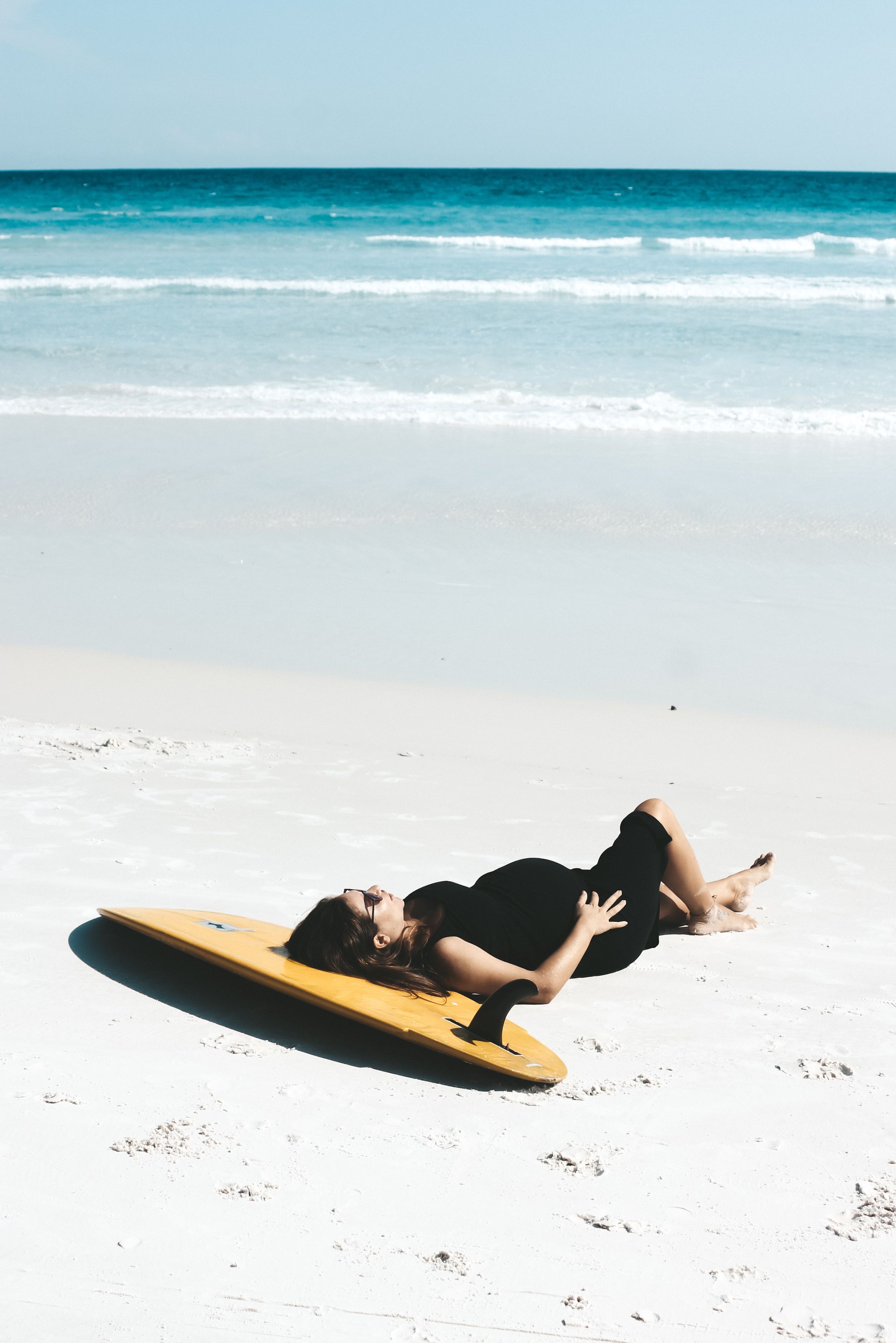 Pregnant Woman in Black Dress Lying on a Surfboard · Free Stock Photo