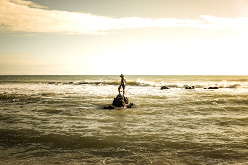 Man Standing on Rock and Fishing in Sea