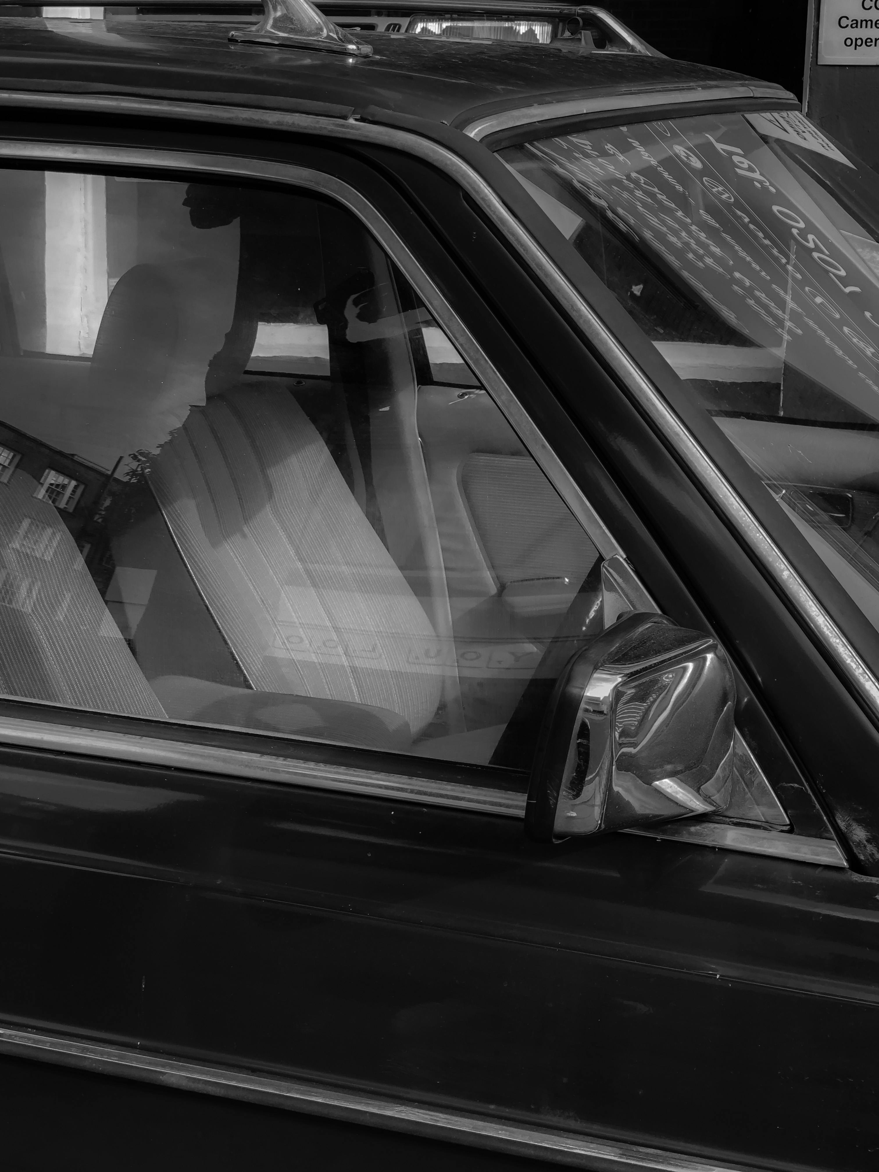 Artistic black and white photo of a vehicle side window with reflections and interior details.