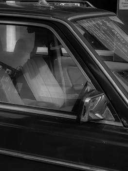 Artistic black and white photo of a vehicle side window with reflections and interior details.