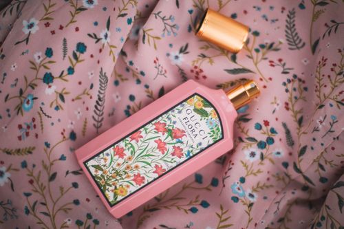 Free A vibrant pink Gucci Flora perfume bottle resting on a floral patterned fabric, showcasing elegance and style. Stock Photo