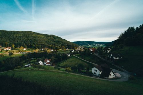 Free Scenic view of a quaint village nestled among lush green hills under a clear sky. Stock Photo