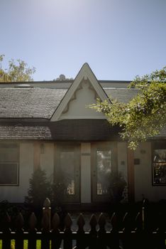 Charming rustic cottage with a unique gabled roof, bathed in sunlight and surrounded by greenery.