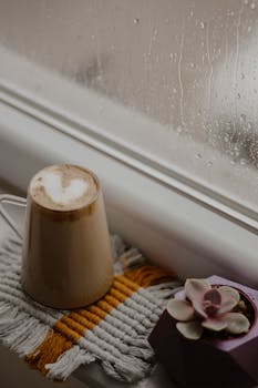 Warm coffee cup on a cozy windowsill during a rainy day, perfect for relaxation.