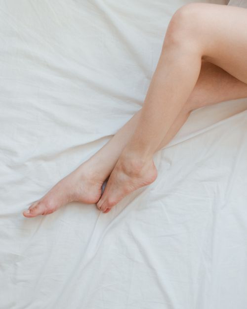 Free Close-up of relaxed female feet on soft white bed sheets, capturing a serene and peaceful moment. Stock Photo
