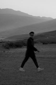 A blurry black and white portrait of a man walking in a mountainous landscape.
