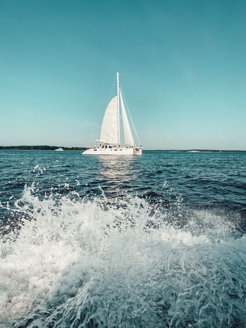 White sailboat on a calm sea with splashing waves and clear blue sky, ideal for travel and adventure themes.