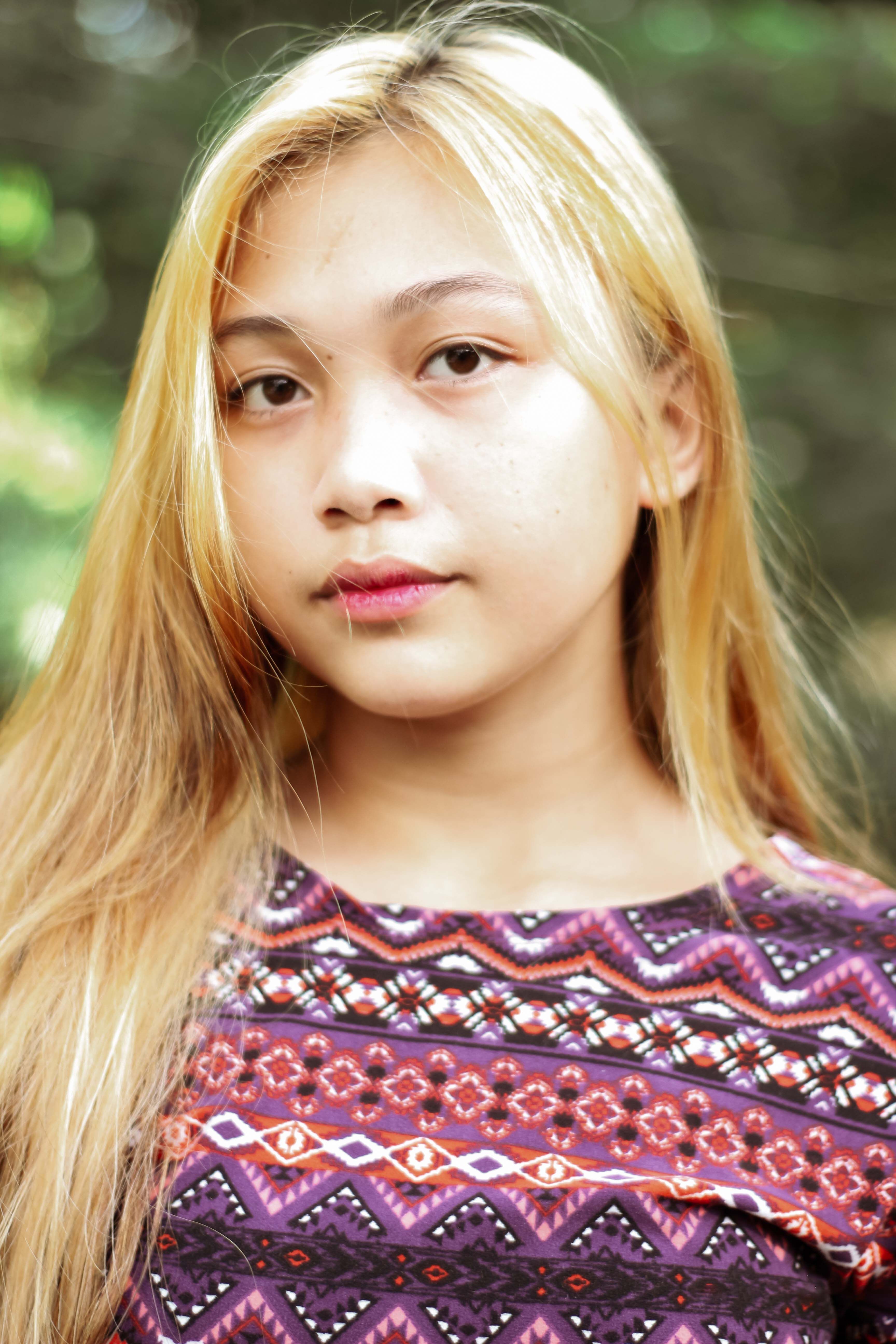 A beautiful blonde Asian woman posing outdoors with a serene expression.
