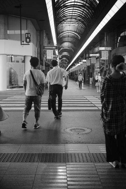 Free Black and white photo capturing pedestrians walking in a train station's urban corridor. Stock Photo
