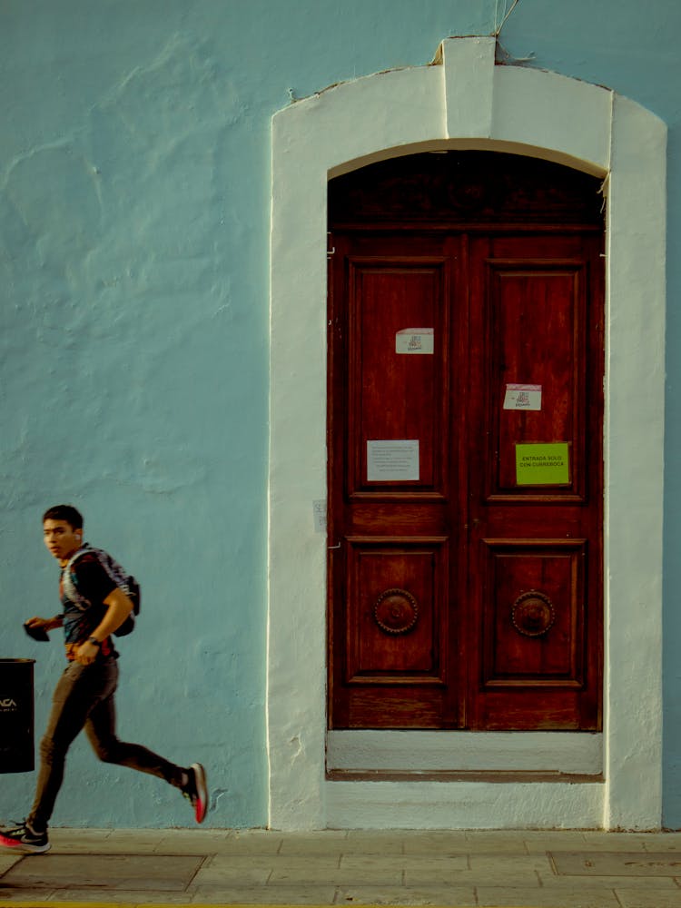 A Man Running On The Sidewalk Near A Door