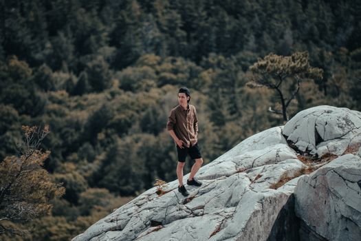 Man Posing on Rocks with Forest Below