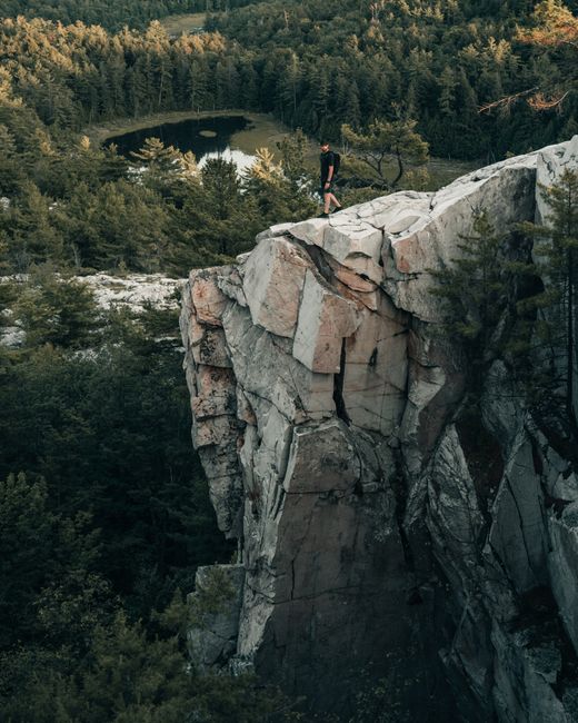 Man stands on rocky cliff edge with forest and lake view, Killarney, Ontario, Canada.