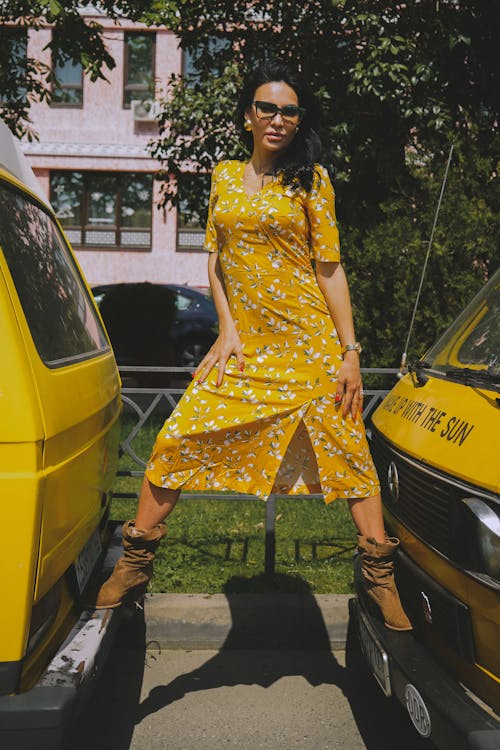 Woman in Floral Dress Standing on the Bumpers of Vehicles