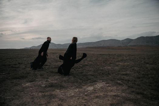 Two people in black attire on a vast, cloudy landscape with mountains.