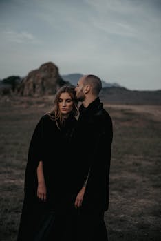 Couple sharing an intimate moment in a moody outdoor setting with rocks and mountains.