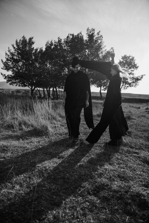 Grayscale Photo of a Man and a Woman Walking on a Grass Field