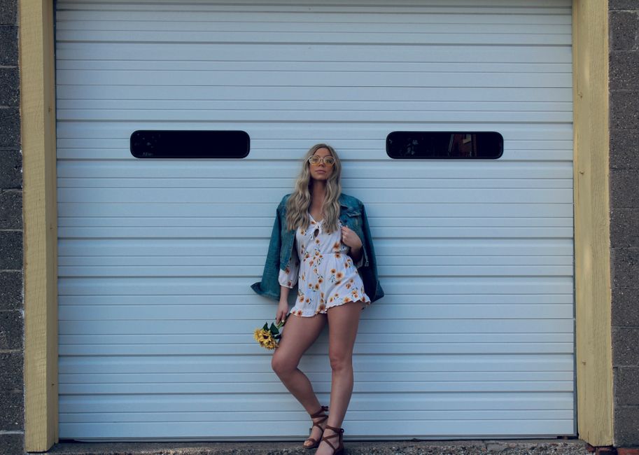 Stylish woman in sunglasses posing against a white garage door in Asbury, IA.