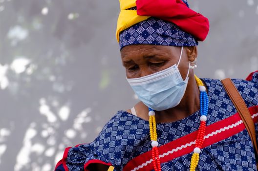 Senior woman wearing a face mask and vibrant traditional clothing outdoors during the day.