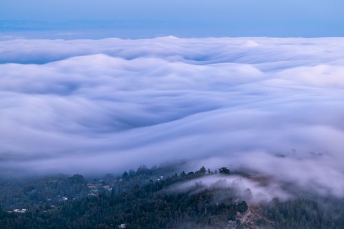 Free A breathtaking aerial view of clouds resembling waves over a mountainous forest landscape. Stock Photo