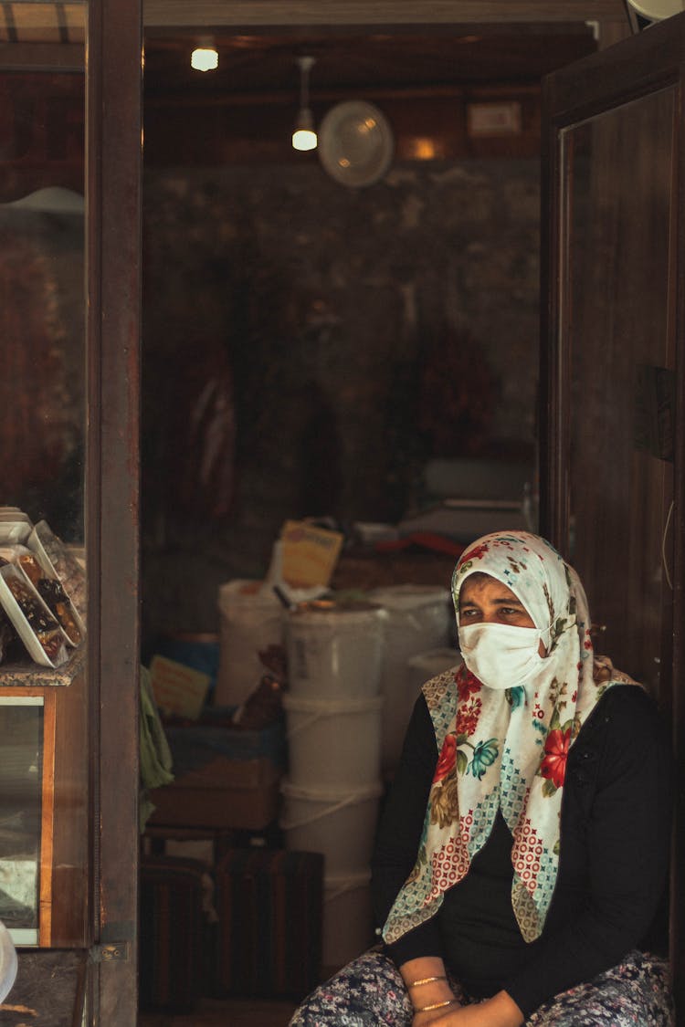 Adult Woman In Traditional Shawl On Head And Corona Mask Sitting In Open Door