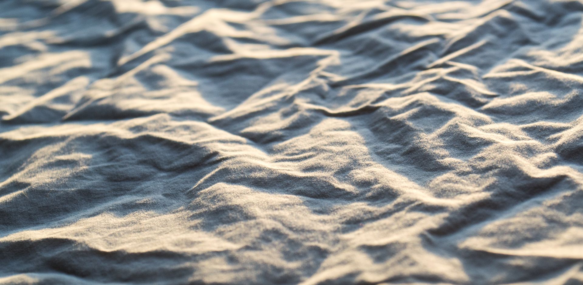 Close-up of wrinkled fabric texture illuminated by soft natural light, creating shadows and patterns.