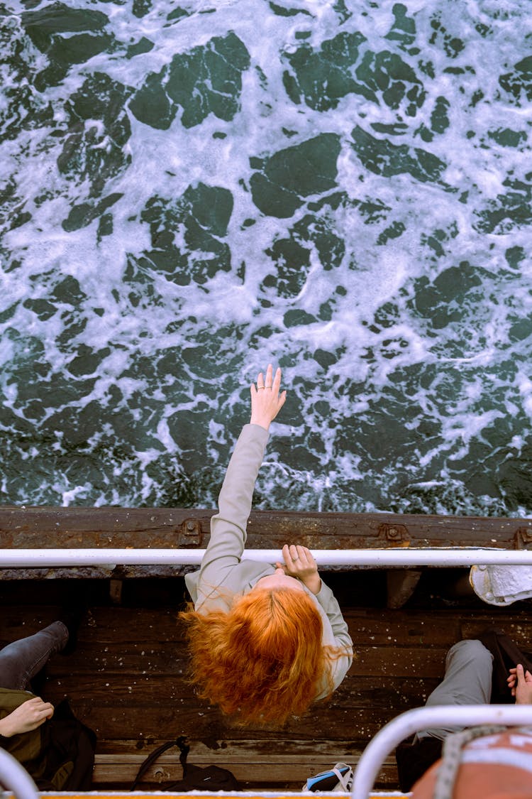 Woman Standing On Board Of Wooden Cruise Ship With Arm Stretched Above Water